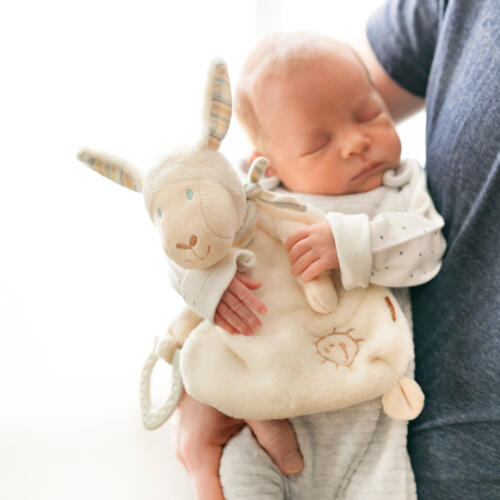 Ein Baby hält das Fehn Schmusetuch Schaf.
