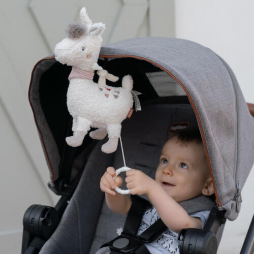 Ein Baby sitzt im Kinderwagen und spielt mit der Spieluhr Lama.