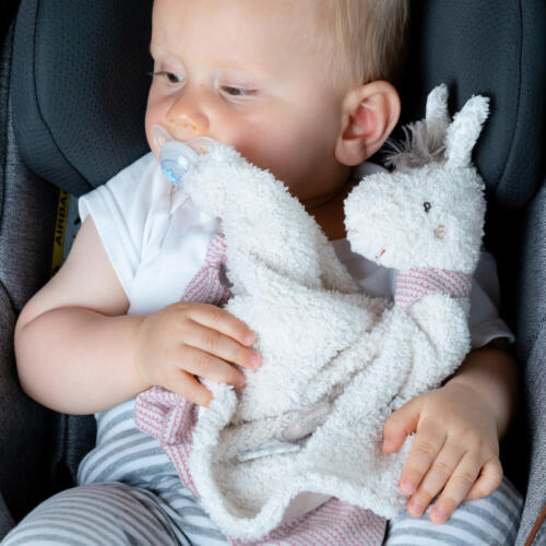 Ein Baby hält das Schmusetuch Lama mit Schnullerhalter und hat seinen Nuckel im Mund.