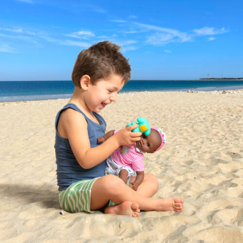 Ein Junge spielt mit einer Puppe, die zum Baden geeignet ist, am Strand.