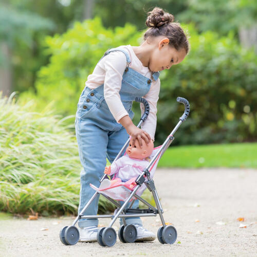 Ein Mädchen spielt mit dem Puppenwagen und fährt ihre Puppe spazieren.