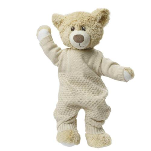 Ein Teddybär trägt den ecrúfarbenen Strickoverall von Heless.